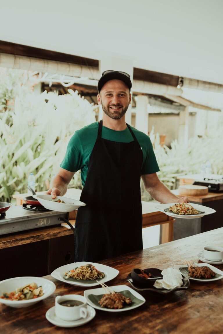 A cheerful chef in Bali showcasing beautifully presented dishes at an outdoor dining setting.