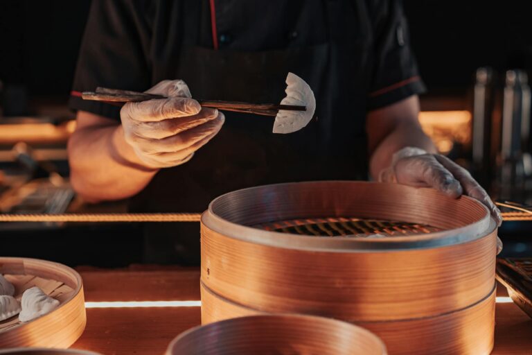 Chef using chopsticks to place dumplings in a bamboo steamer for cooking.